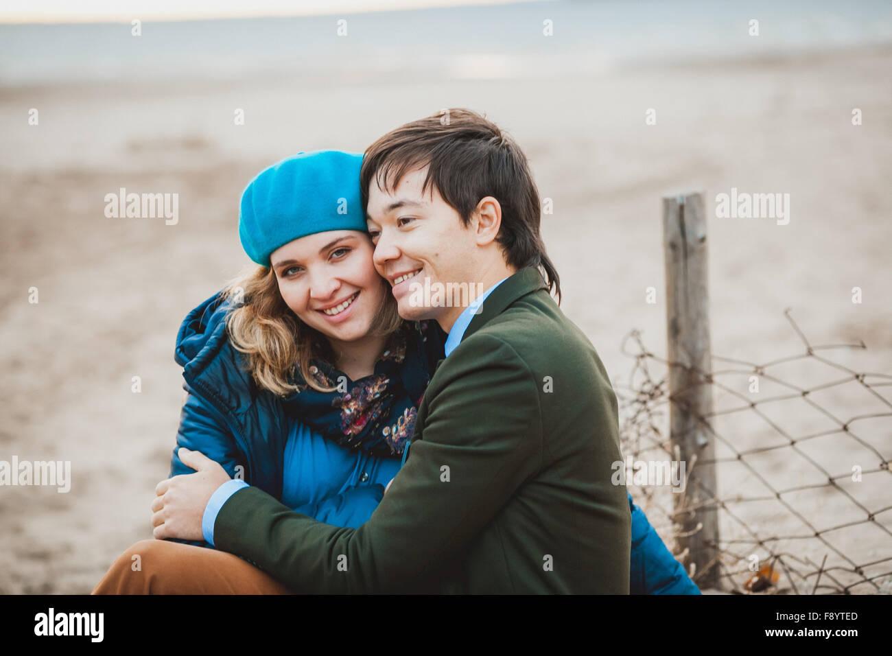 junges Paar sitzt und posiert am Strand im Herbst Stockfoto