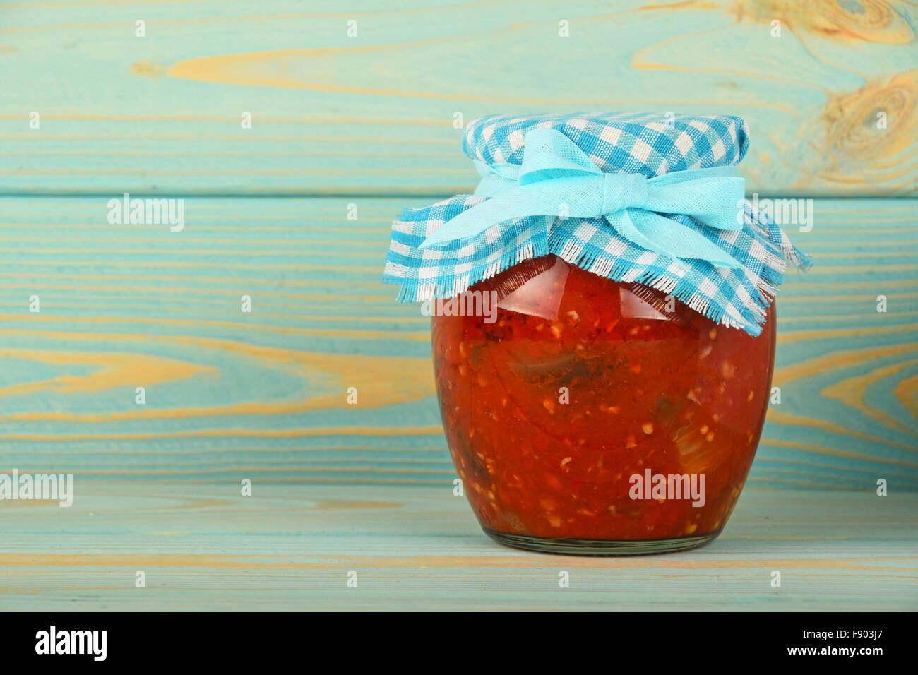 Ein Glas hausgemachte eingelegte Pfeffer, Paprika und Auberginen Salat mit kariertem Textil Top Dekoration blau lackierten vinta Stockfoto