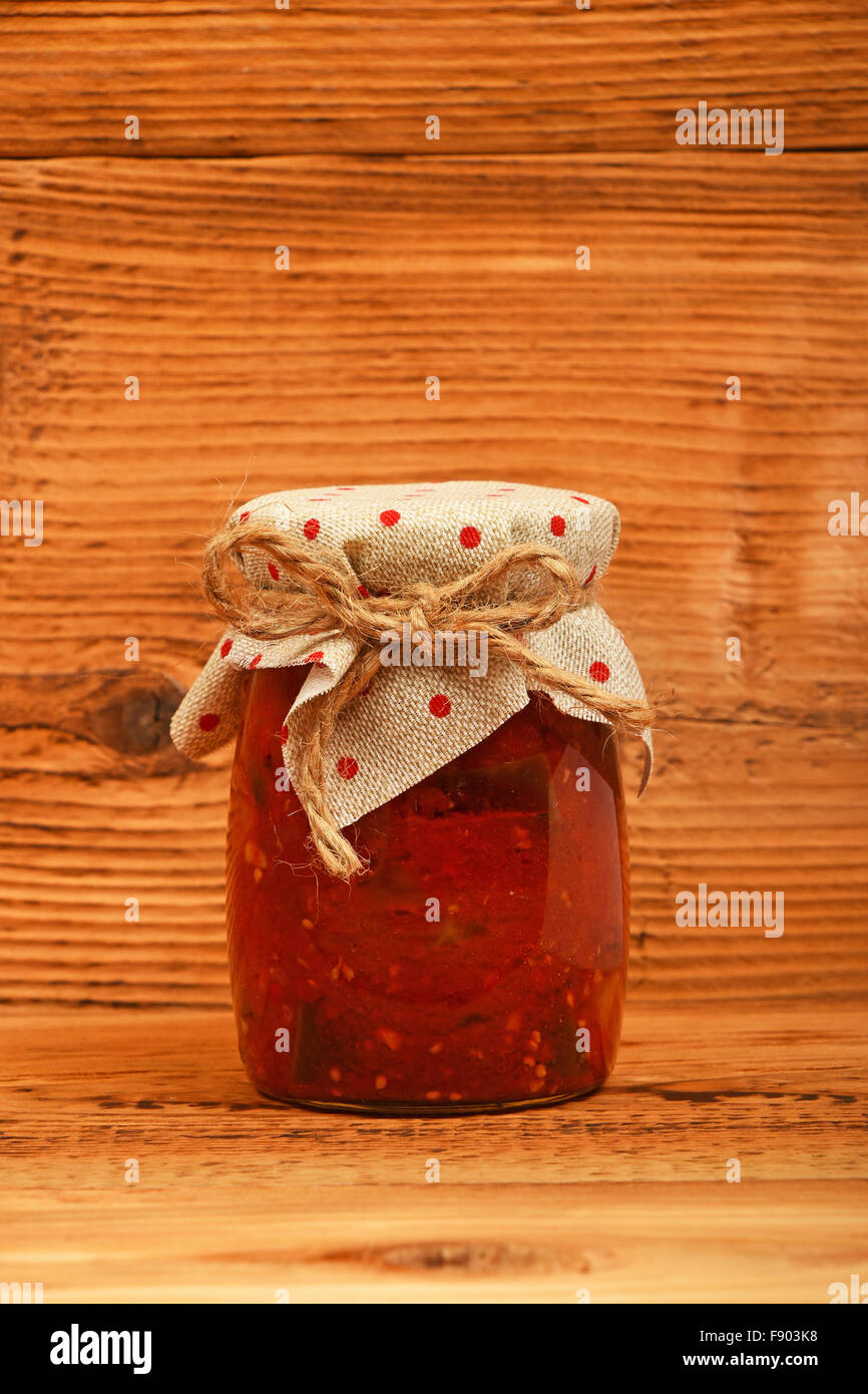Ein Glas hausgemachte eingelegte Pfeffer, Paprika und Auberginen Salat mit gepunkteten Textildekoration bei Holz braun Vintage top Stockfoto