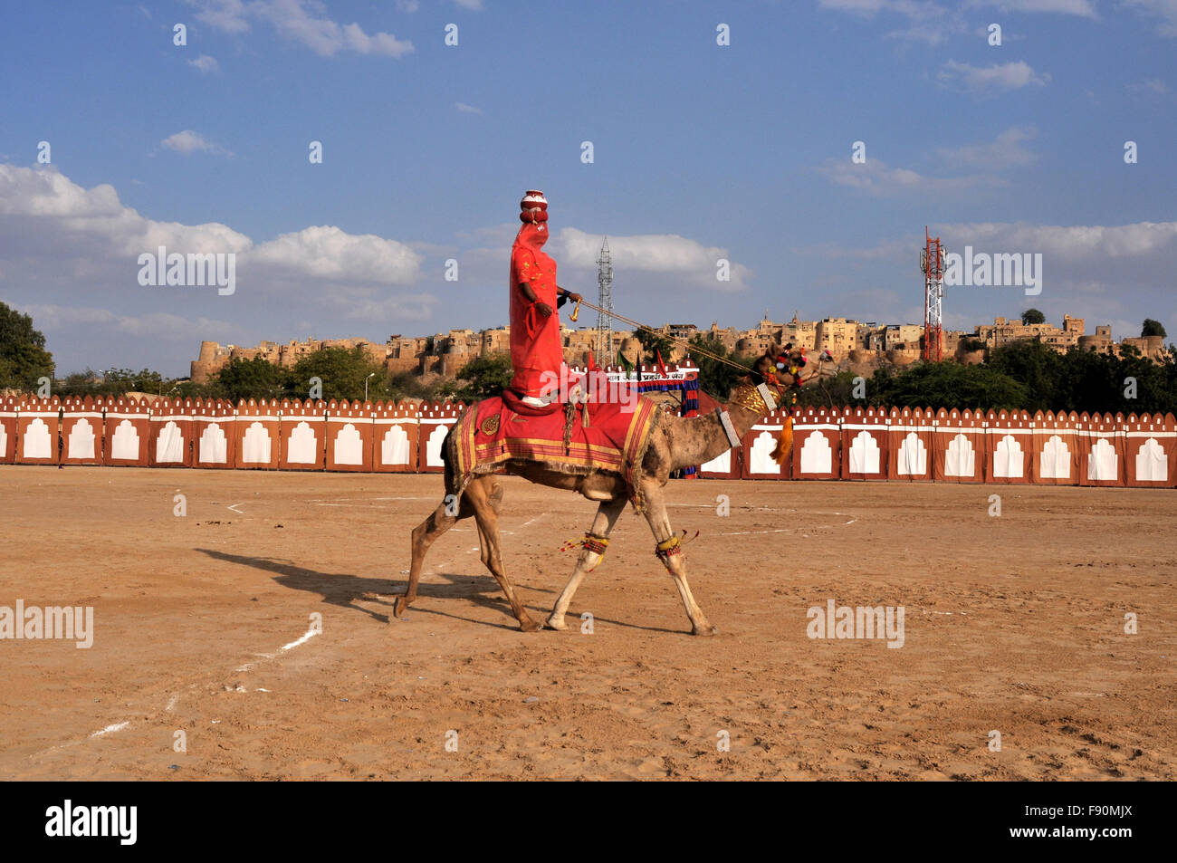 Eine Frau, die Durchführung mit einer Matka auf dem Kopf auf dem Kamel zurück während das Jaisalmer Wüste Festival in Jaisalmer, Rajasthan, Indien. Stockfoto