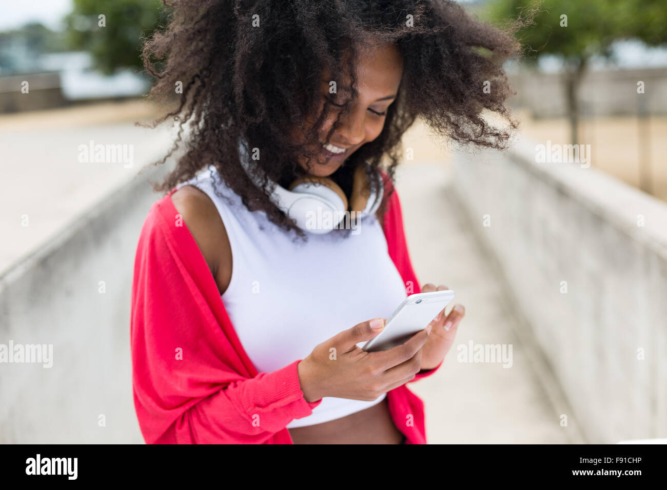 Eine junge Mischenrennen Frau anhören von Musik auf einem Smartphone mit Kopfhörern im freien Stockfoto