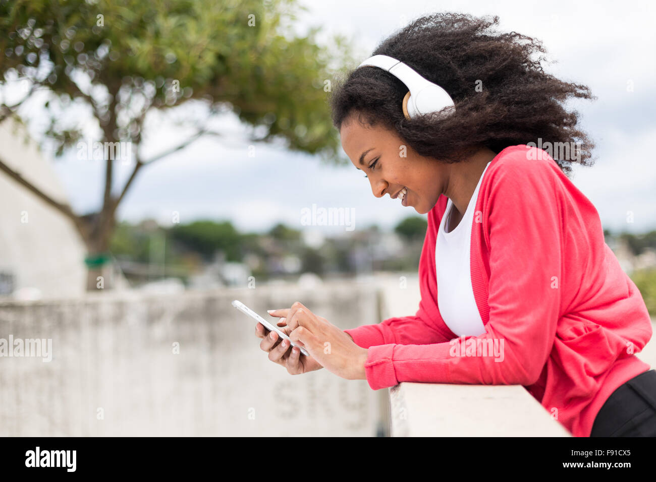 Eine junge Mischenrennen Frau anhören von Musik auf einem Smartphone mit Kopfhörern im freien Stockfoto