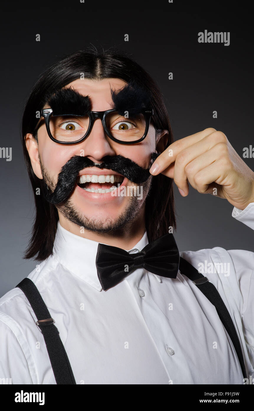 Junger Mann mit falschen Schnurrbart und Augenbrauen isoliert auf grau Stockfoto