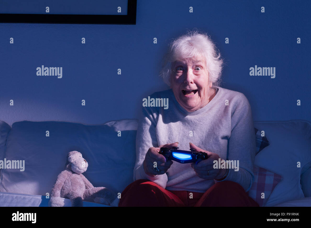 Ältere Dame sitzt auf einem Sofa auf einer Playstation 4 neben ein Stofftier Affe spielen. Stockfoto