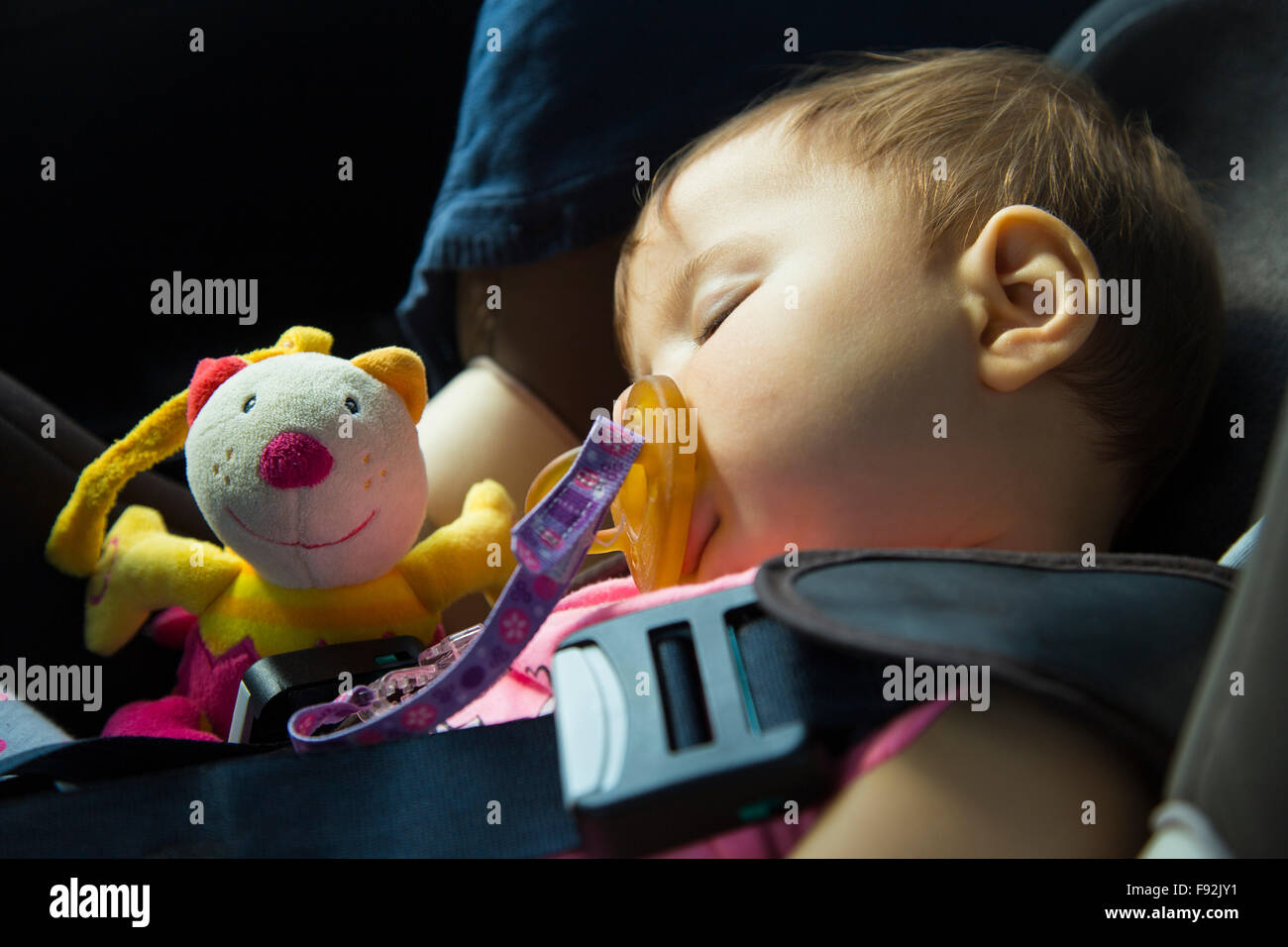 9 Monate altes Babymädchen schläft in den Autositz mit ihrer Puppe Stockfoto