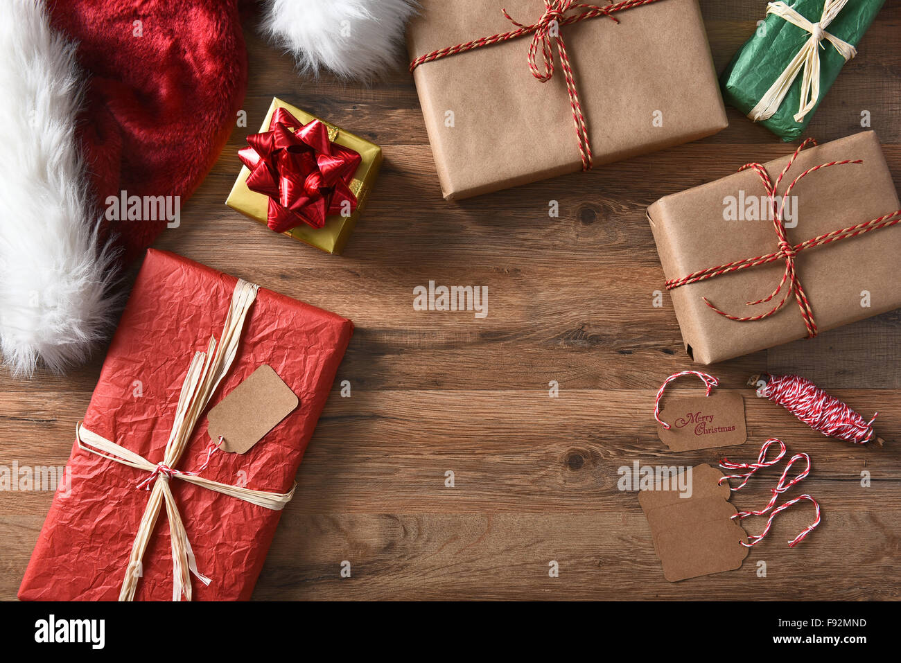Draufsicht des umschlossenen Weihnachten präsentiert auf einem rustikalen Holztisch mit String, Geschenkanhänger und Weihnachtsmütze. Querformat mit Stockfoto