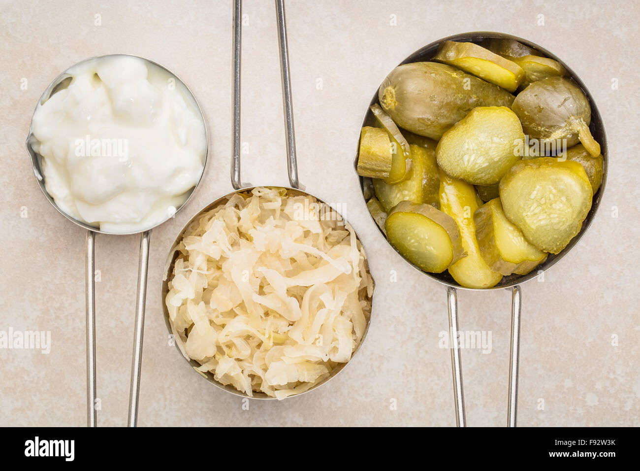 Sauerkraut, Gurken Essiggurken und Joghurt - fermentiert beliebte probiotische Lebensmittel - drei Messbecher gegen keramische Fliesen Stockfoto