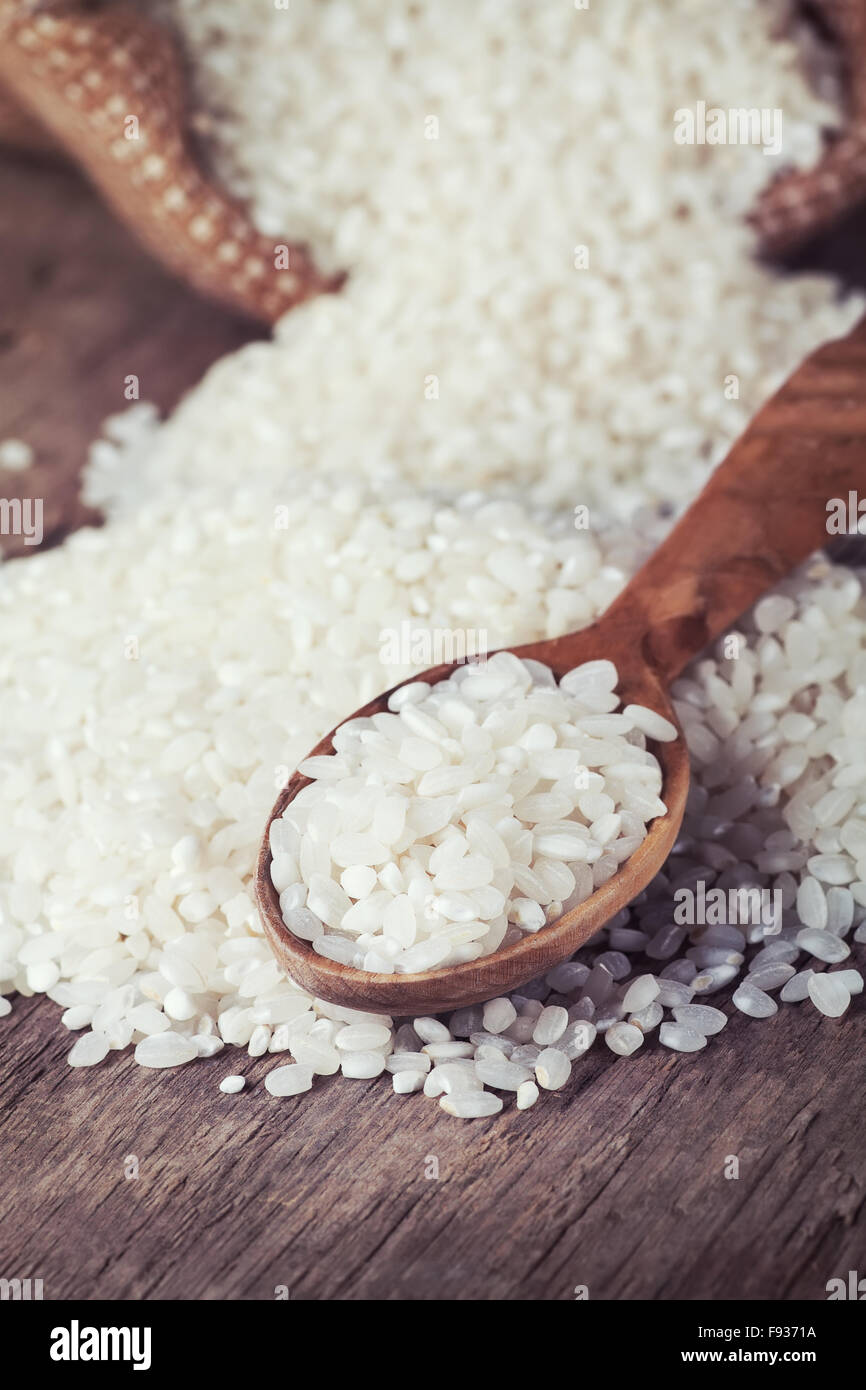 Weißer Reis Spill aus Jute Beutel und Holzlöffel auf dem Holztisch Stockfoto