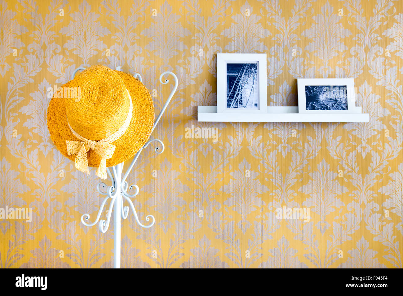 Gelbe Strohhut auf einem Kleiderständer und ein Regal mit schwarz / weiß Bilder Stockfoto