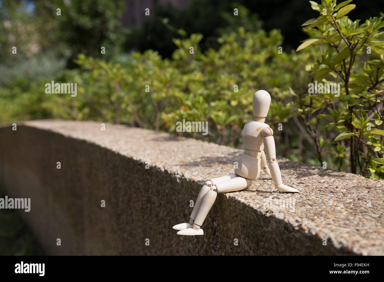 Junge Holzpuppe entspannt in der Sonne auf einer Wand mit Pflanzen-Hintergrund Stockfoto