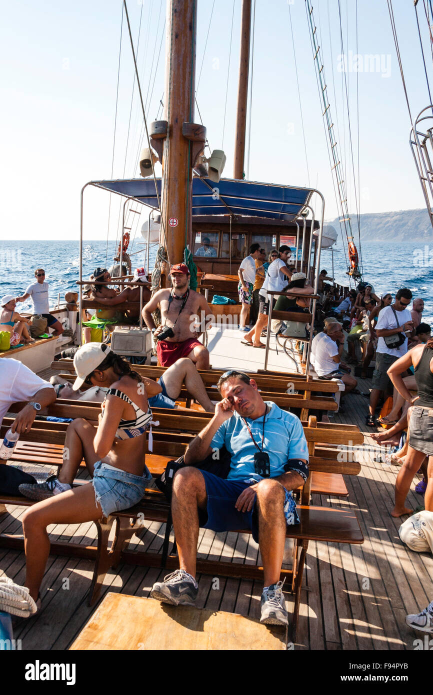 Santorini Thira. Bow View zum Heck der Touristen an Deck Exkursion Boot zu Nea Kameni, einige sitzen einige stehend, Mann vor eingeschlafen. Stockfoto Santorini Thira. Bow View zum Heck der Touristen an Deck Exkursion Boot zu Nea Kameni, einige sitzen einige stehend, Mann vor eingeschlafen. Stockfoto
