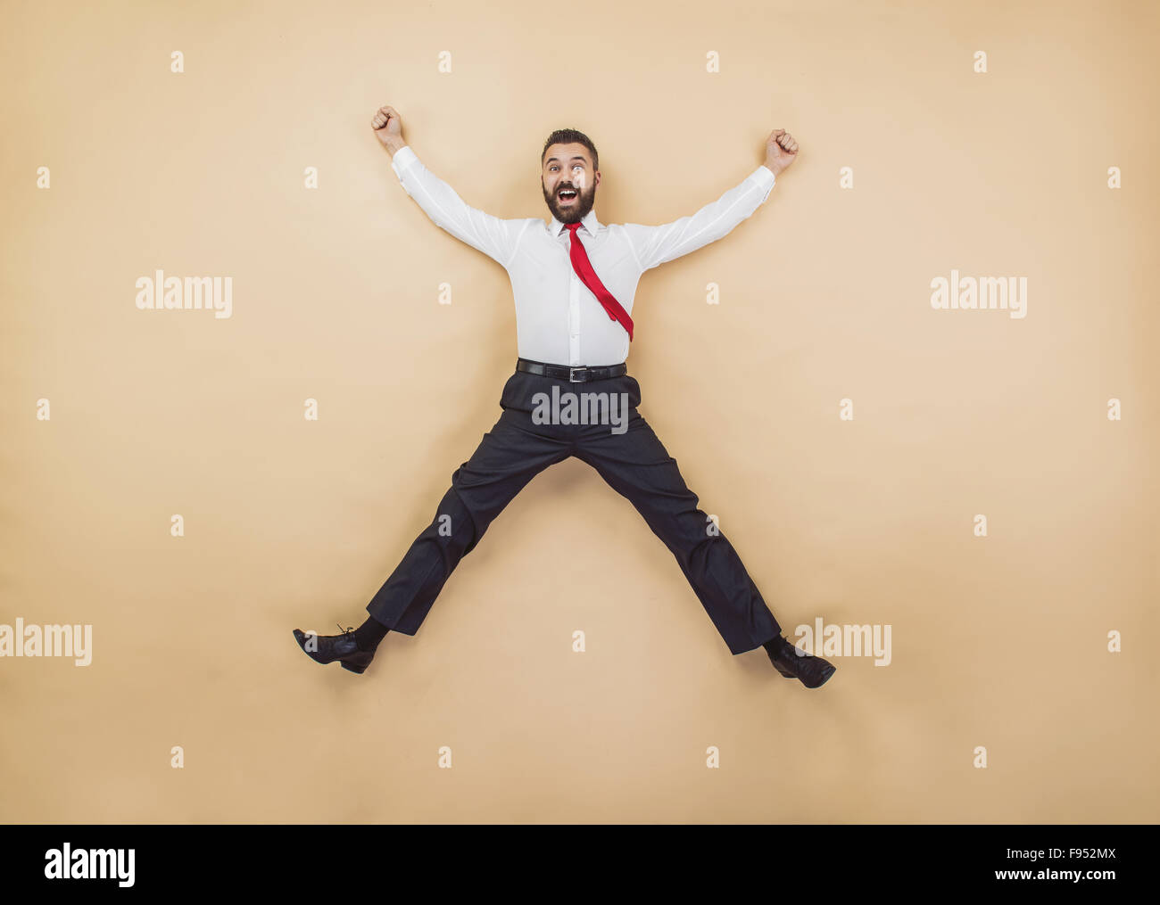 Glücklich-Manager in einer siegreichen Pose hoch springen. Studio auf einem beigen Hintergrund gedreht. Stockfoto