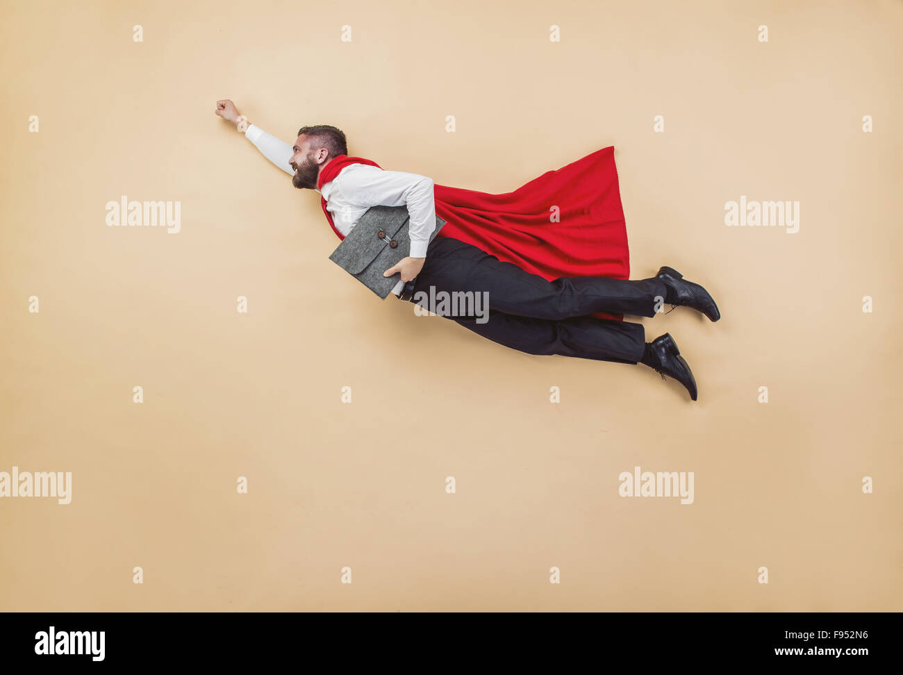 Manager in einer Superman-Pose tragen einen roten Mantel. Studio auf einem beigen Hintergrund gedreht. Stockfoto