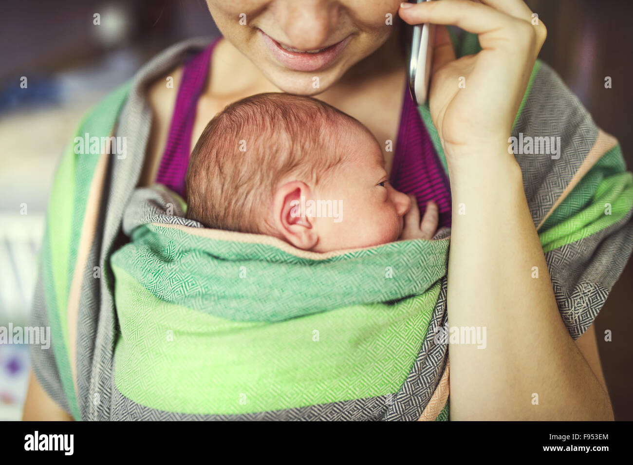 Neugeborenes Baby Halt von Mutter in der Babytrage wickeln. Mama am Telefon anrufen. Stockfoto