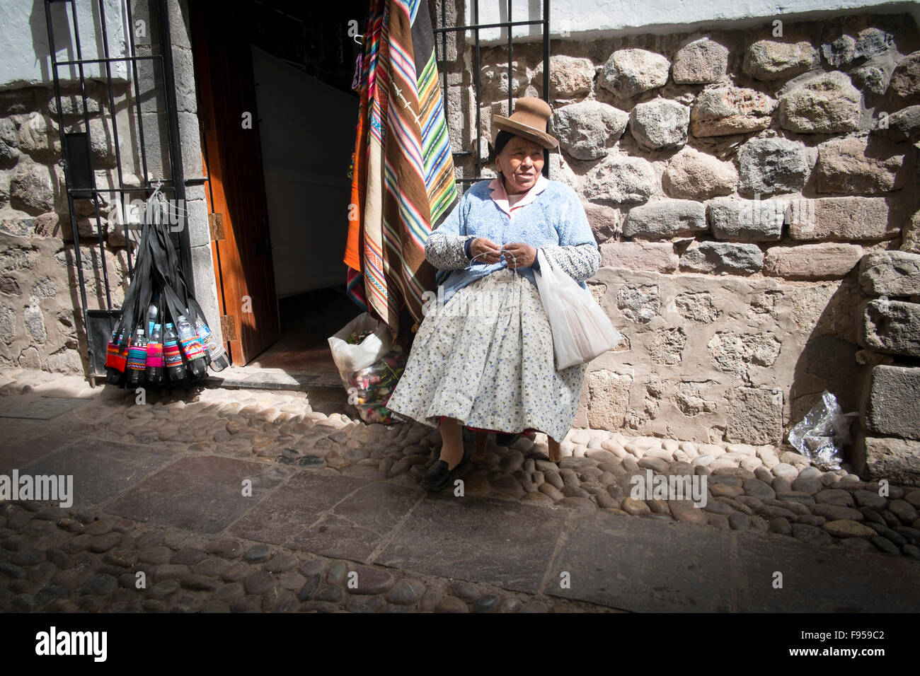 Cusco, Peru. Eine Frau sitzt auf einer kleinen Seitenstraße in der Sonne. Stockfoto