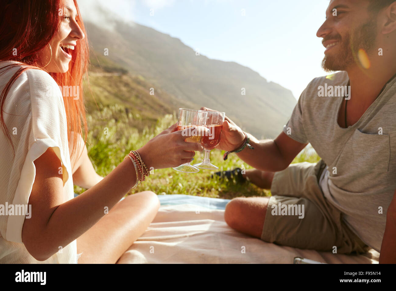 Aufnahme eines fröhlichen jungen Paares Wein trinken und genießen ein Picknick.  Junger Mann mit ihrer Freundin im Urlaub auf dem Rasen sitzen Stockfoto