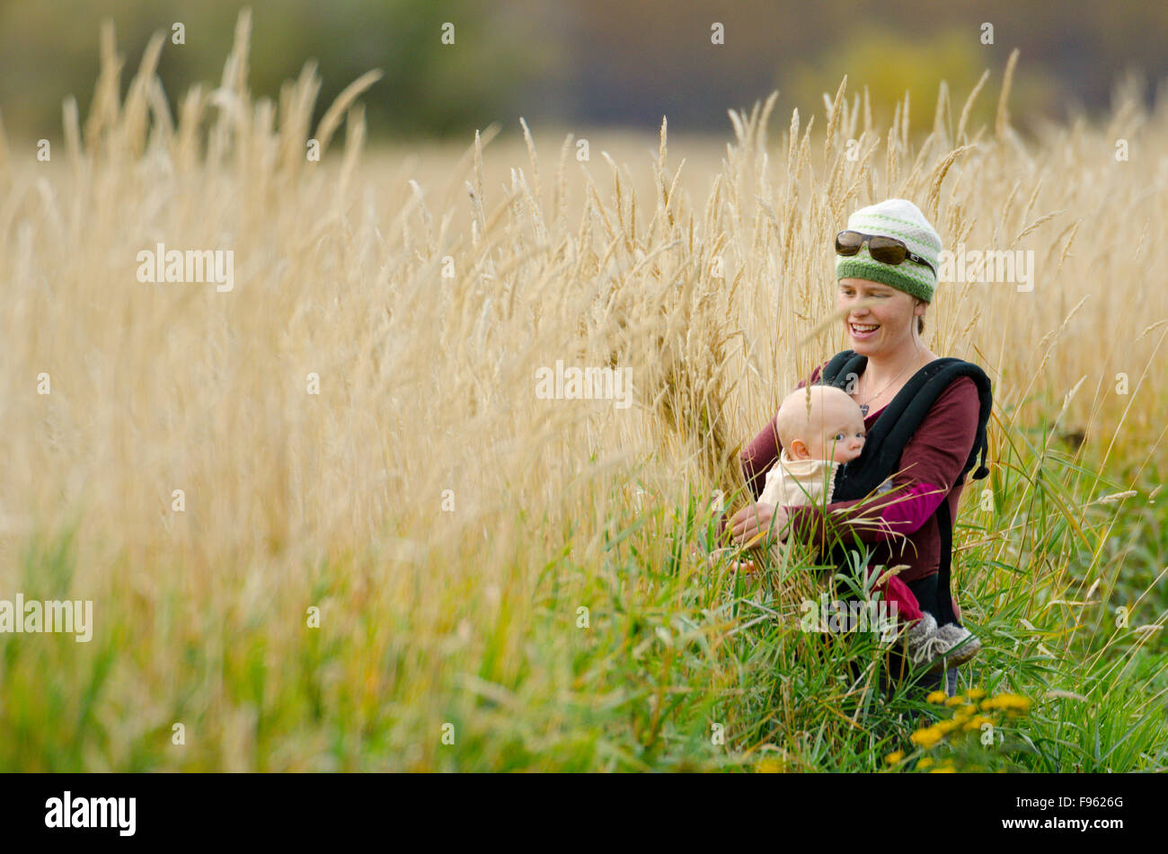 Eine junge Mutter trägt ihr Baby beim Sammeln von Rasen für Zierpflanzen, Creston, Britisch-Kolumbien Stockfoto
