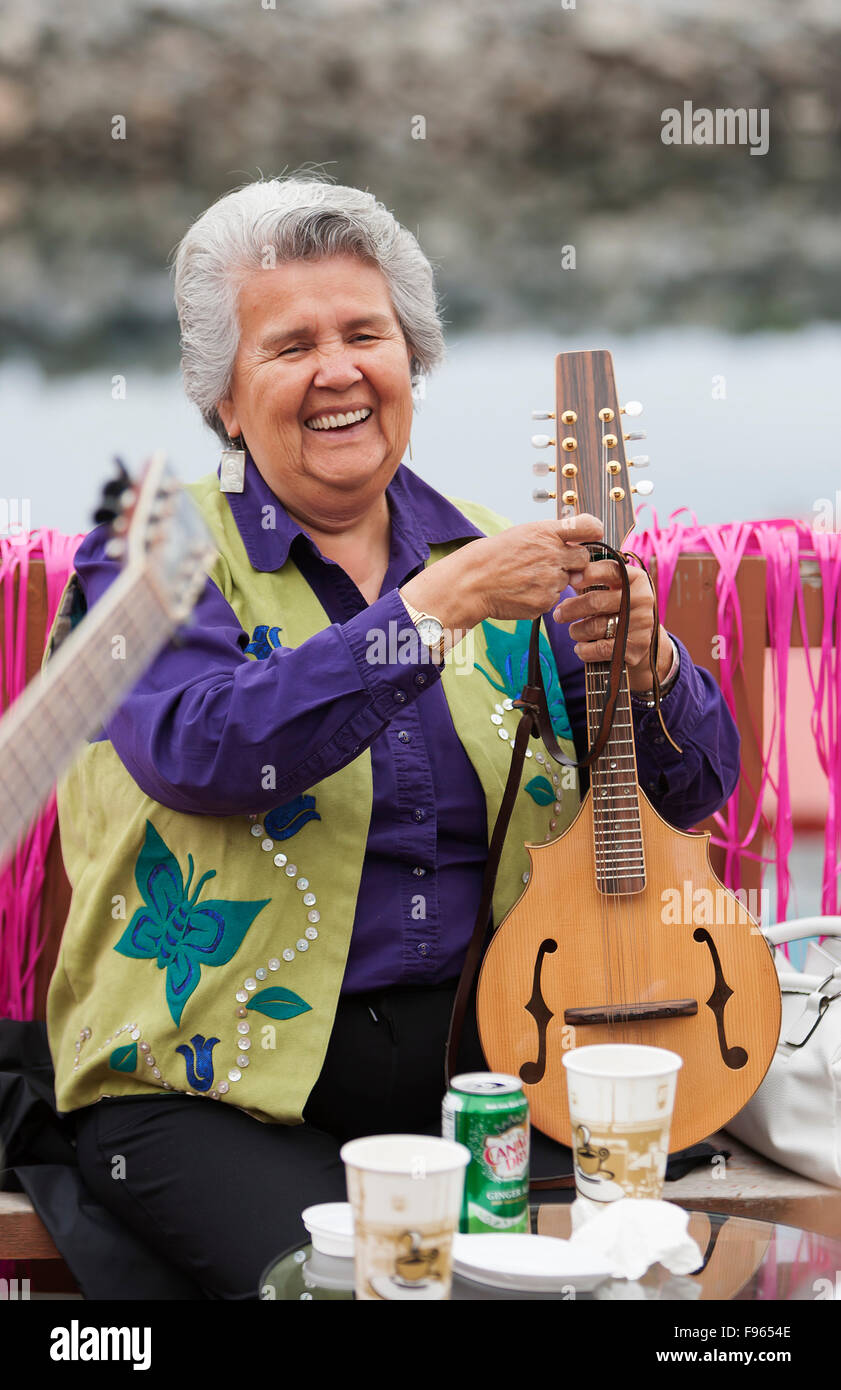 Eine lächelnde ältere erste Nationen senior passt ihre Mandoline während einer musikalischen Versammlung der ersten Nationen Freunde auf dem Deck des ein Stockfoto