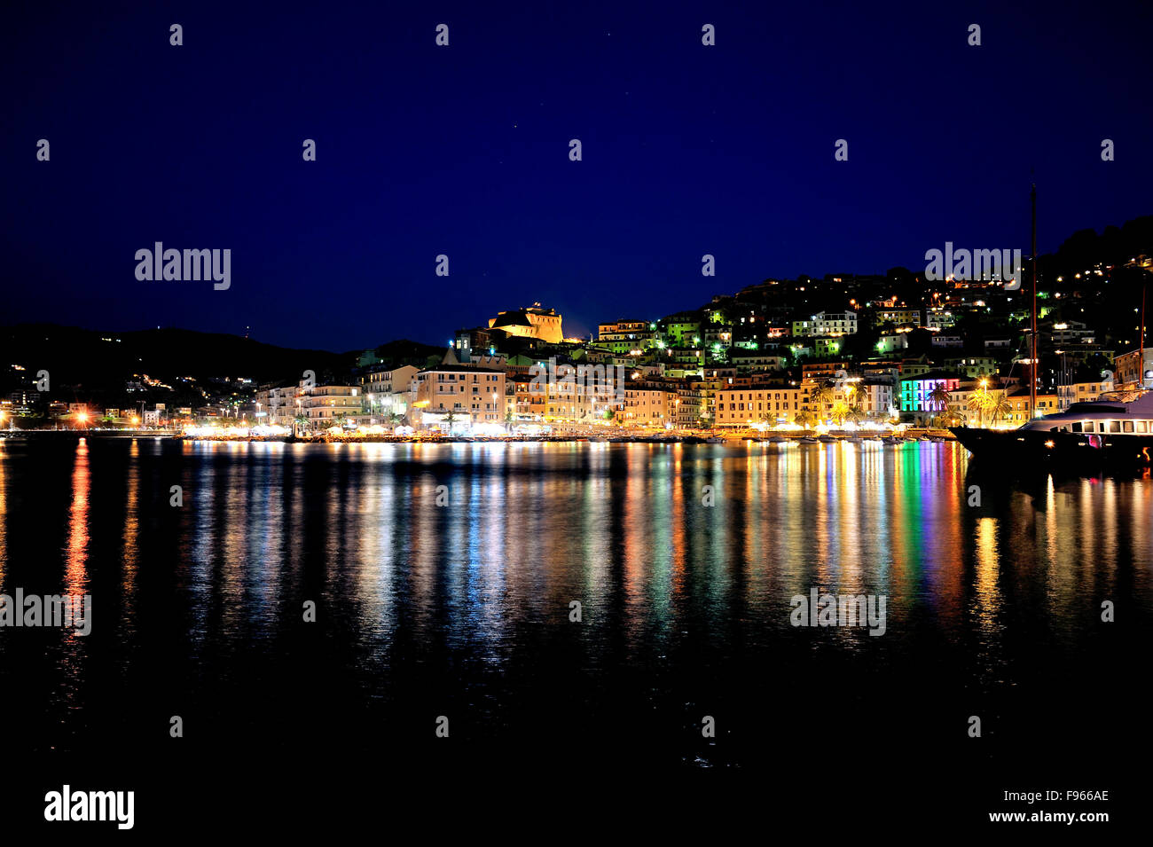 Night Shot Panorama, bunte Beleuchtung in der Nacht mit Reflexion im Hafen der Stadt Porto Santo Stefano, an der Küste der Toskana, Italien Stockfoto