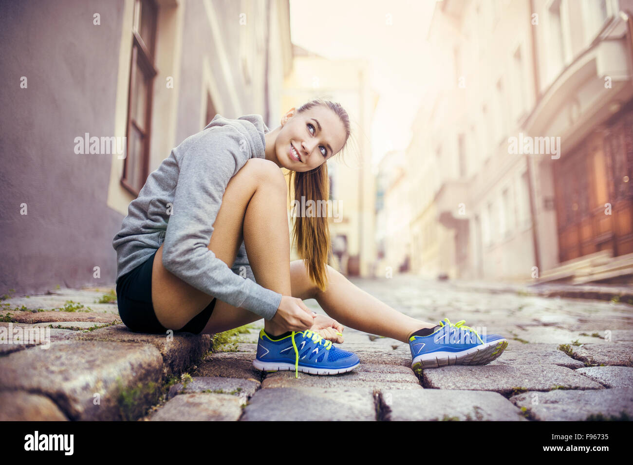Junge weibliche Läufer ist ihre Laufschuhe auf gefliesten Bürgersteig im alten Stadtzentrum binden. Stockfoto