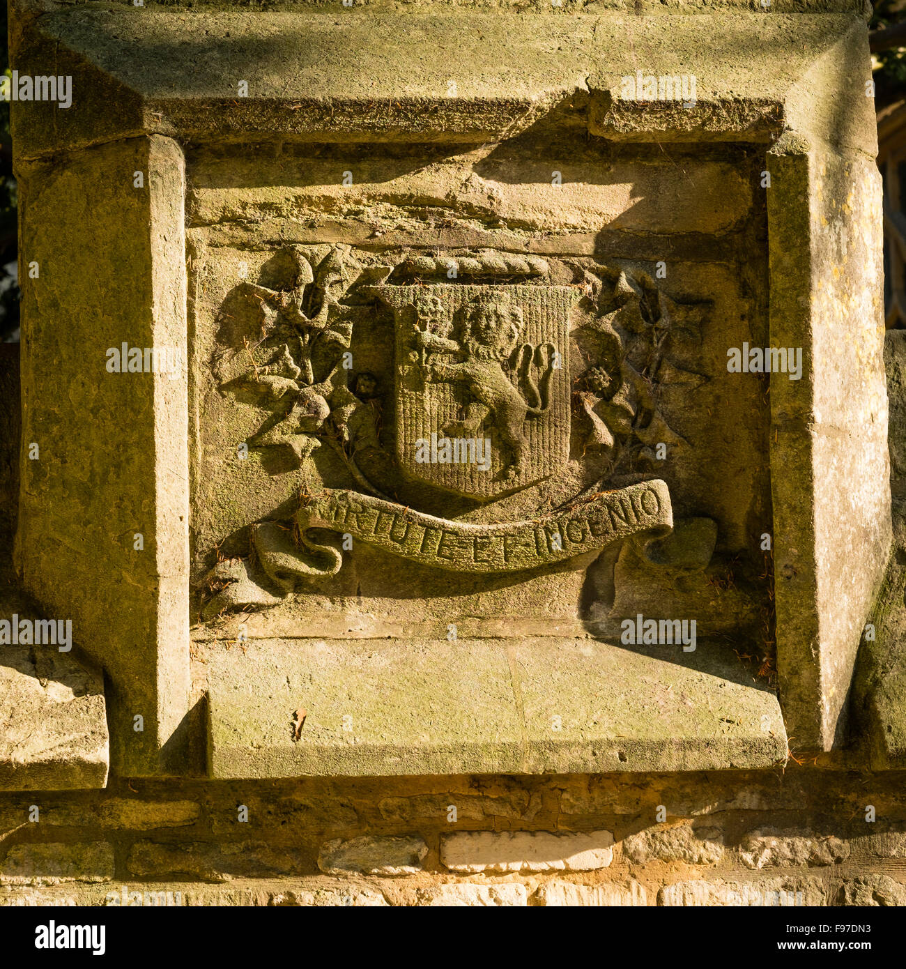 Stone panel mit Wappen mit Löwen auf Schild und Motto VIRTUTE ET INGENIO - durch Tugend und Fähigkeit: geschnitzte Sandstein Motto und Emblem an der Wand der Pfarrkirche in Cirencester, Gloucestershire, England, UK Stockfoto