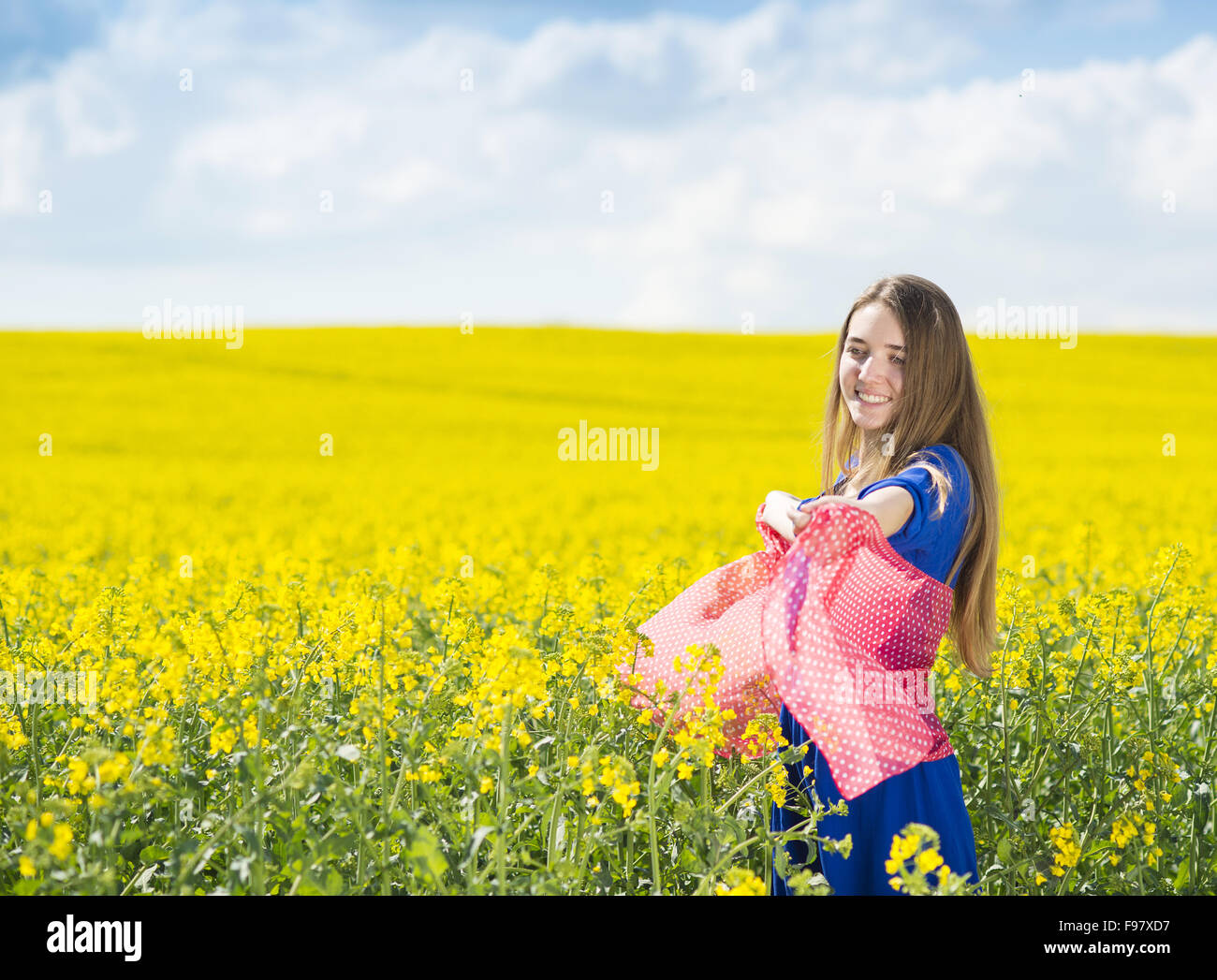 Fröhliches junges Mädchen im blauen Kleid und roten Schal in gelben Raps Feld Freizeit genießen Stockfoto