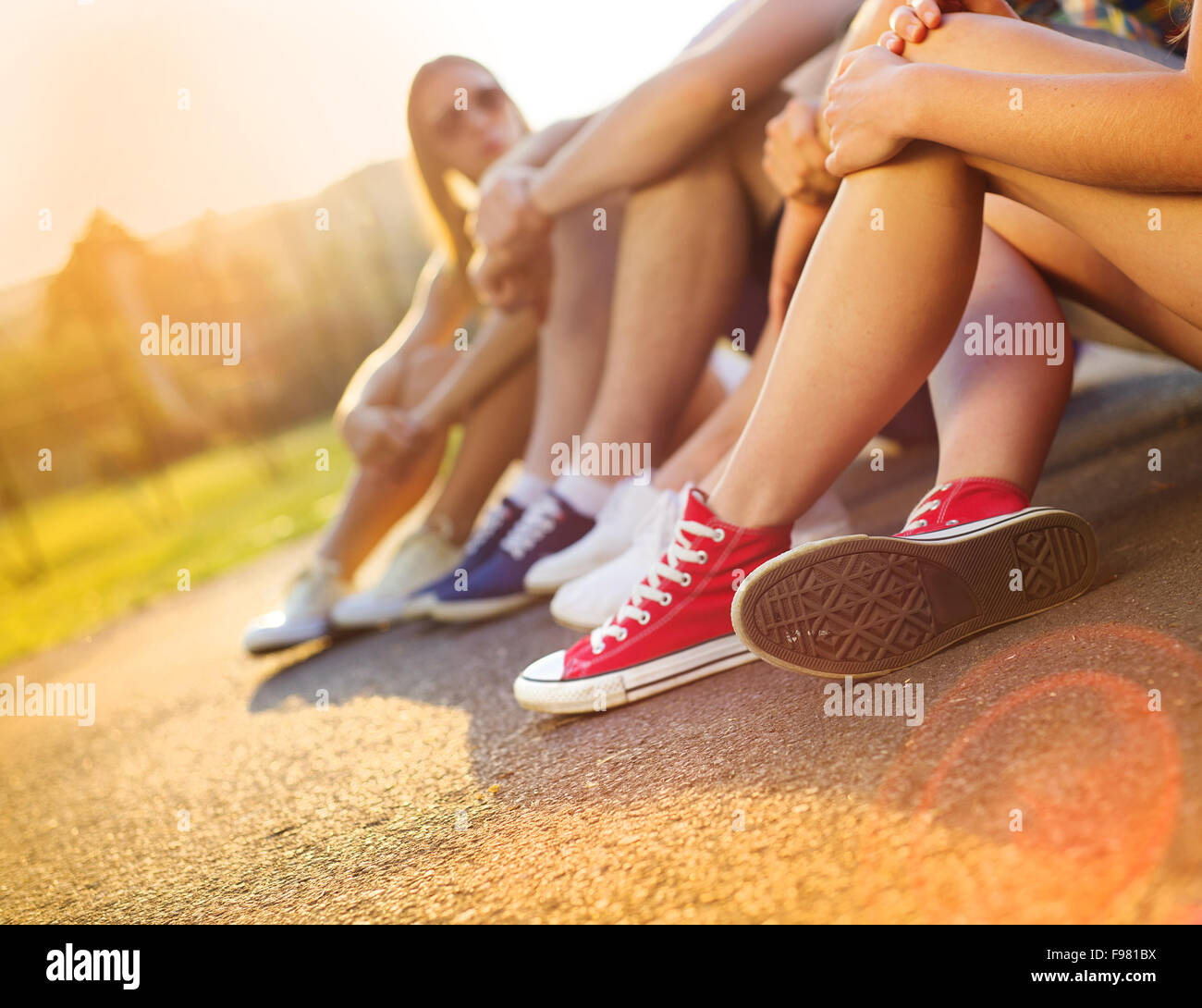Beine und Sneakers von Teenager-Jungen und Mädchen sitzen auf dem Bürgersteig Stockfoto