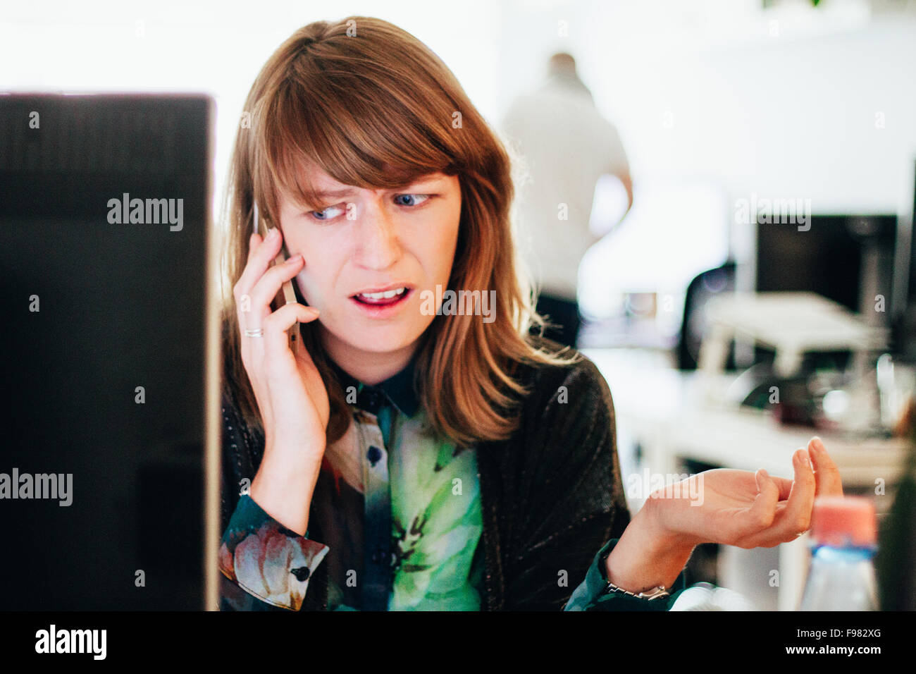 Besorgt Frau am Handy beim Sitzen am Computer-Schreibtisch im Büro Stockfoto