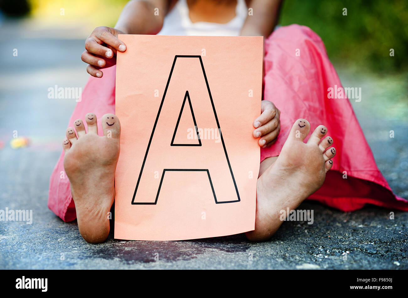 Nahaufnahme der niedliche kleine Mädchen zeigt Buchstaben A in sonnigen, grünen park Stockfoto