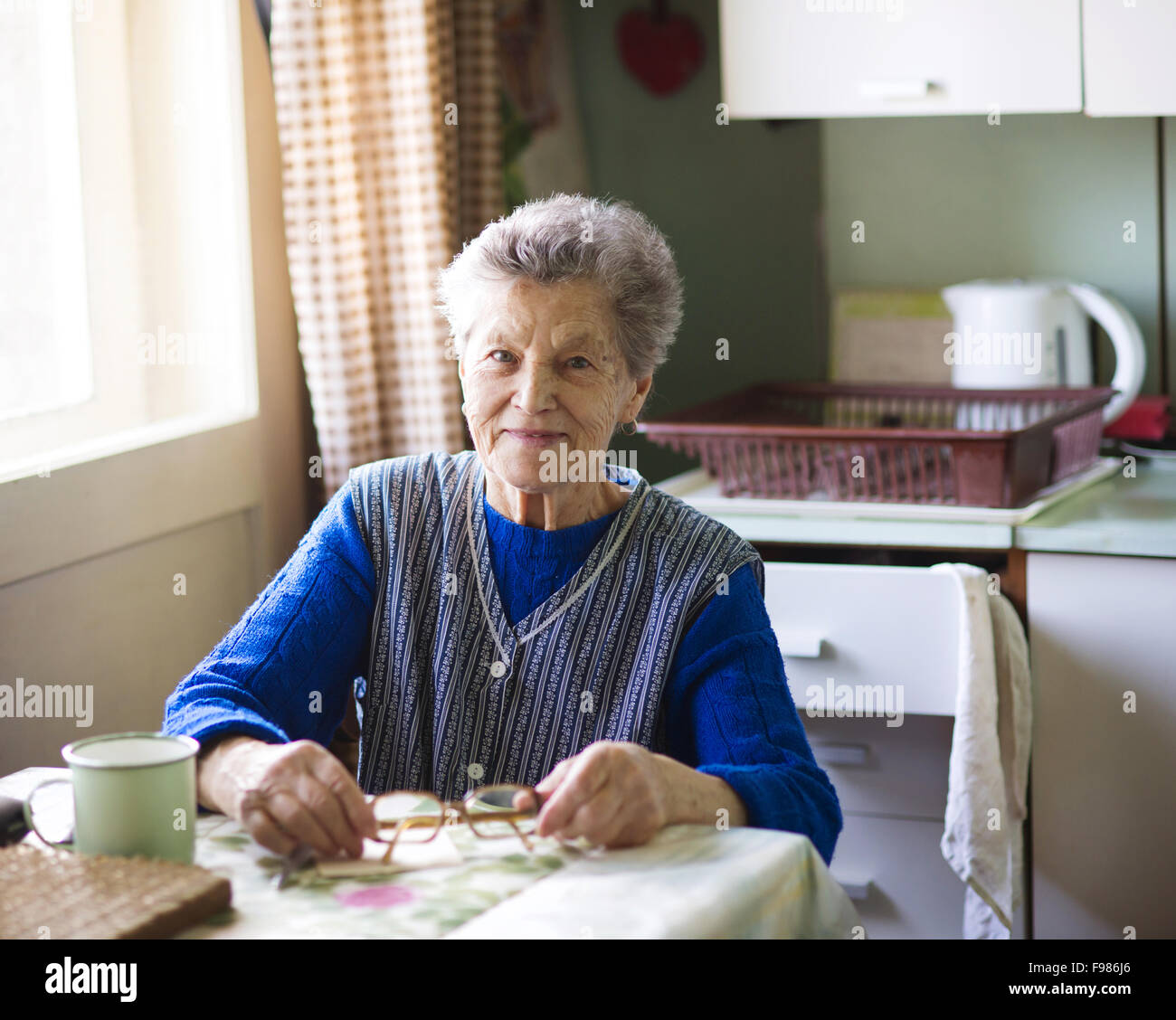 Alte Frau sitzt in ihrer Landhausküche Stockfoto