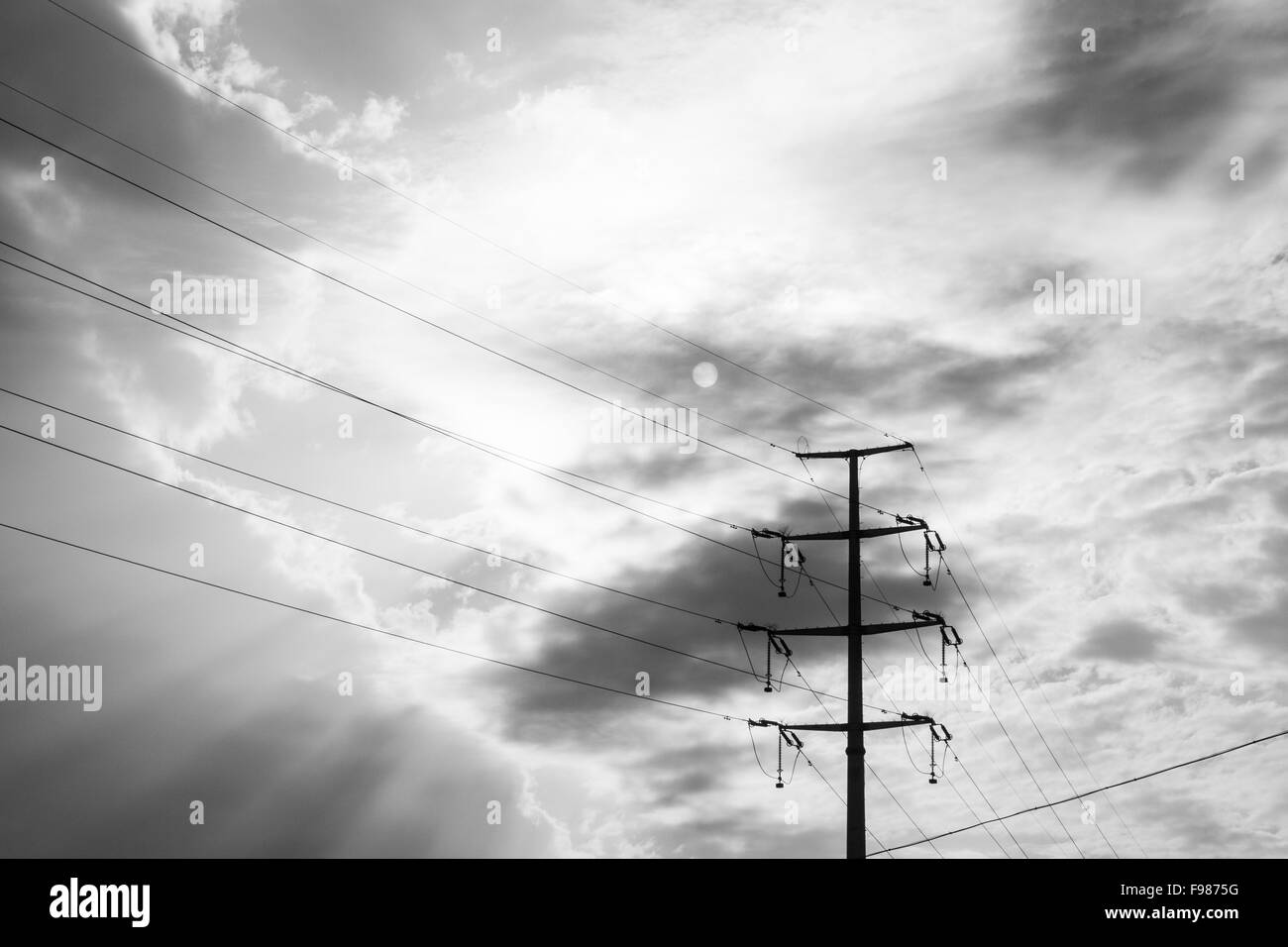 Strommast in bedrohlichen Wetterbedingungen, schwarze Wolken und die Sonne Stockfoto