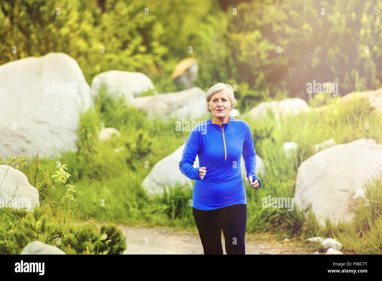 Ältere Frau, Joggen in der wunderschönen Natur, Felsen im Hintergrund Stockfoto