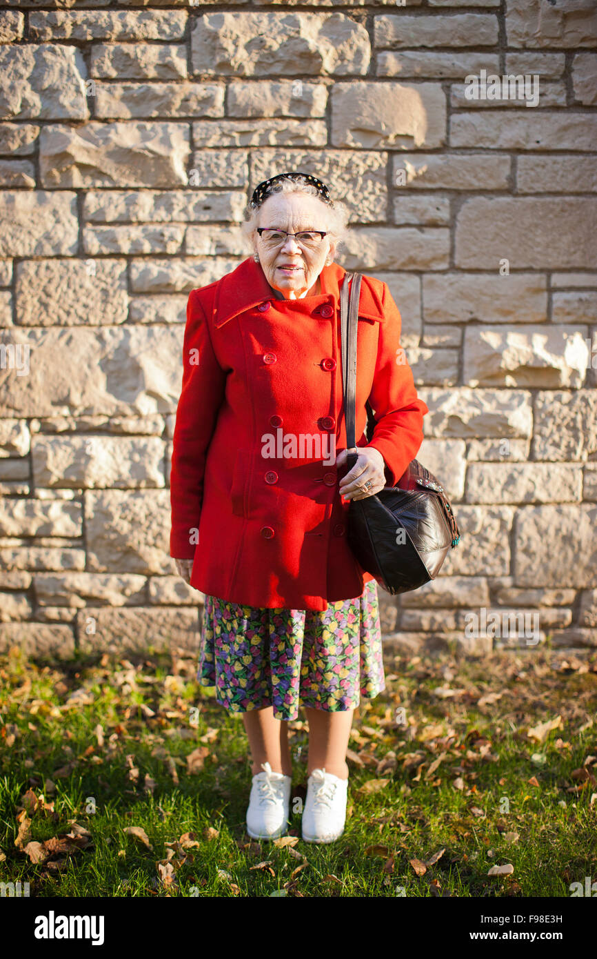 Eine ältere Frau trägt eine rote Jacke steht gegen eine Mauer. Stockfoto