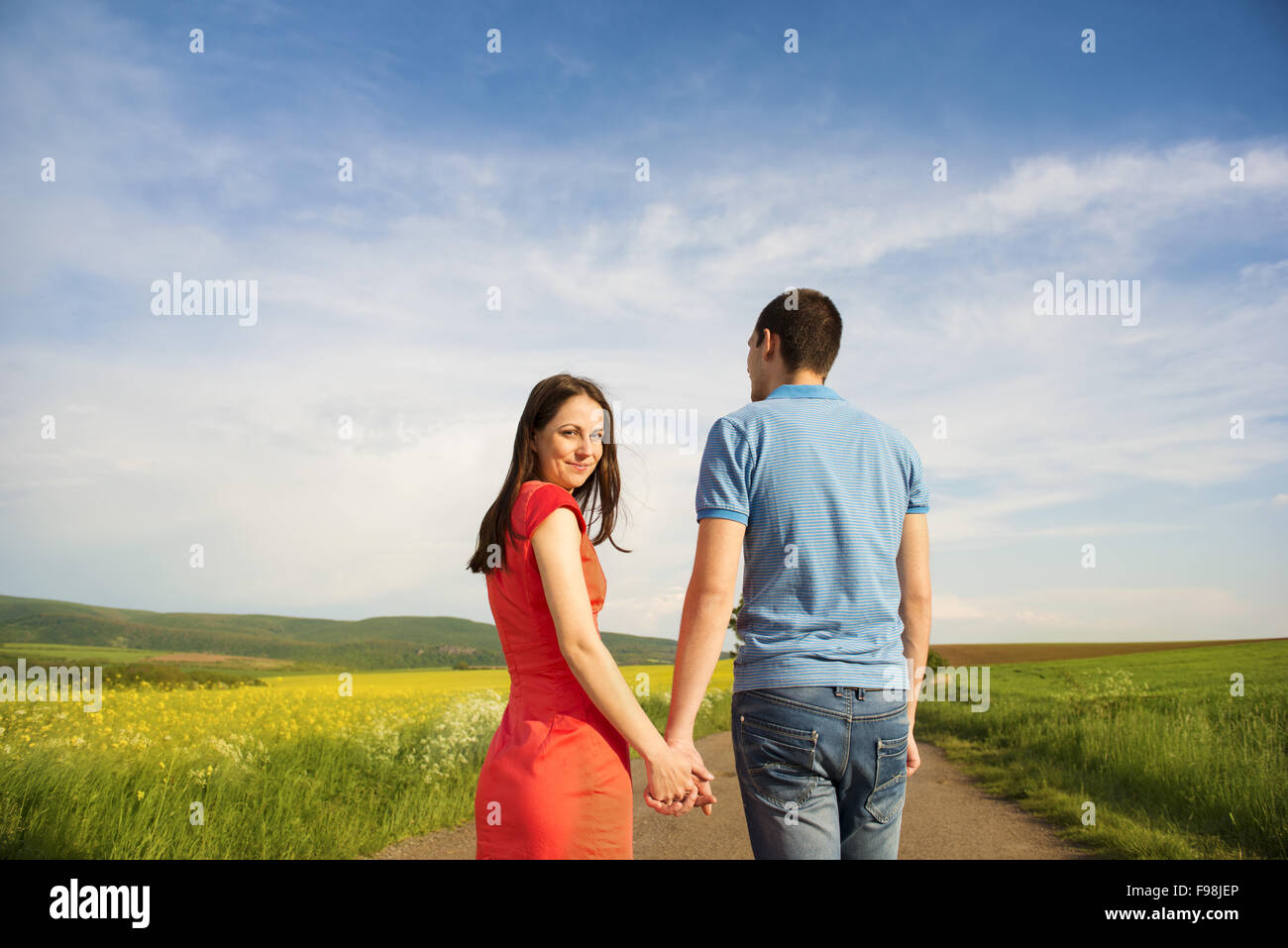 Glückliches junges Paar in Liebe zu Fuß und Hand in Hand unterwegs Landschaft neben dem Raps Feld Stockfoto