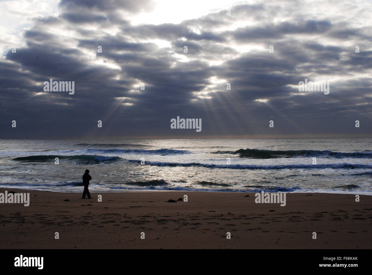 Mann geht zum Meer am dunklen Sandstrand unter schönen bewölkten Himmel Stockfoto