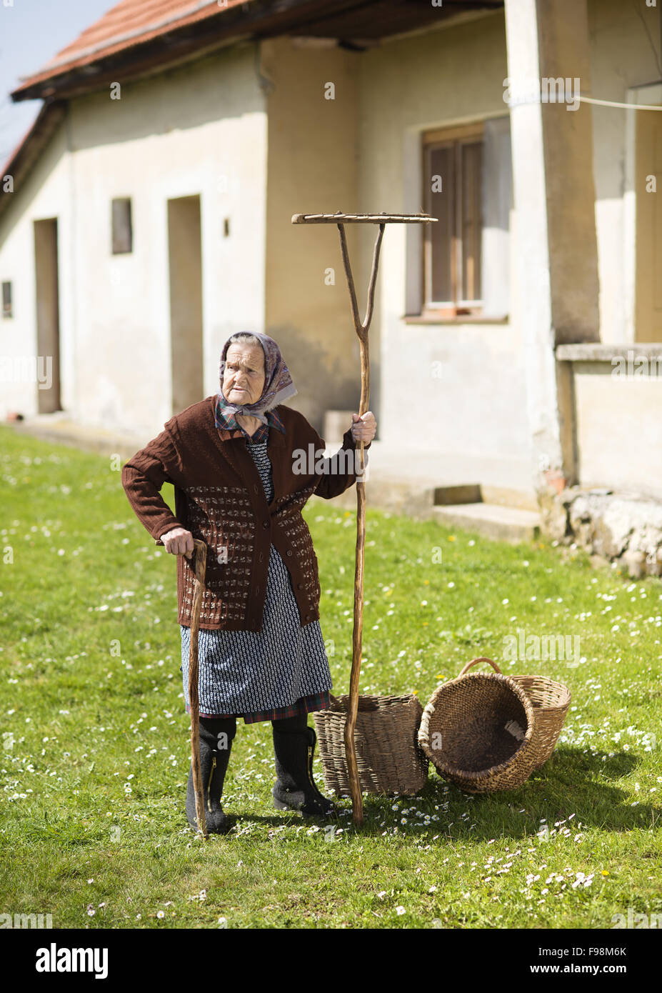 Sehr alte Frau im Kopftuch mit Gartengeräten in ihrem Hinterhof Stockfoto