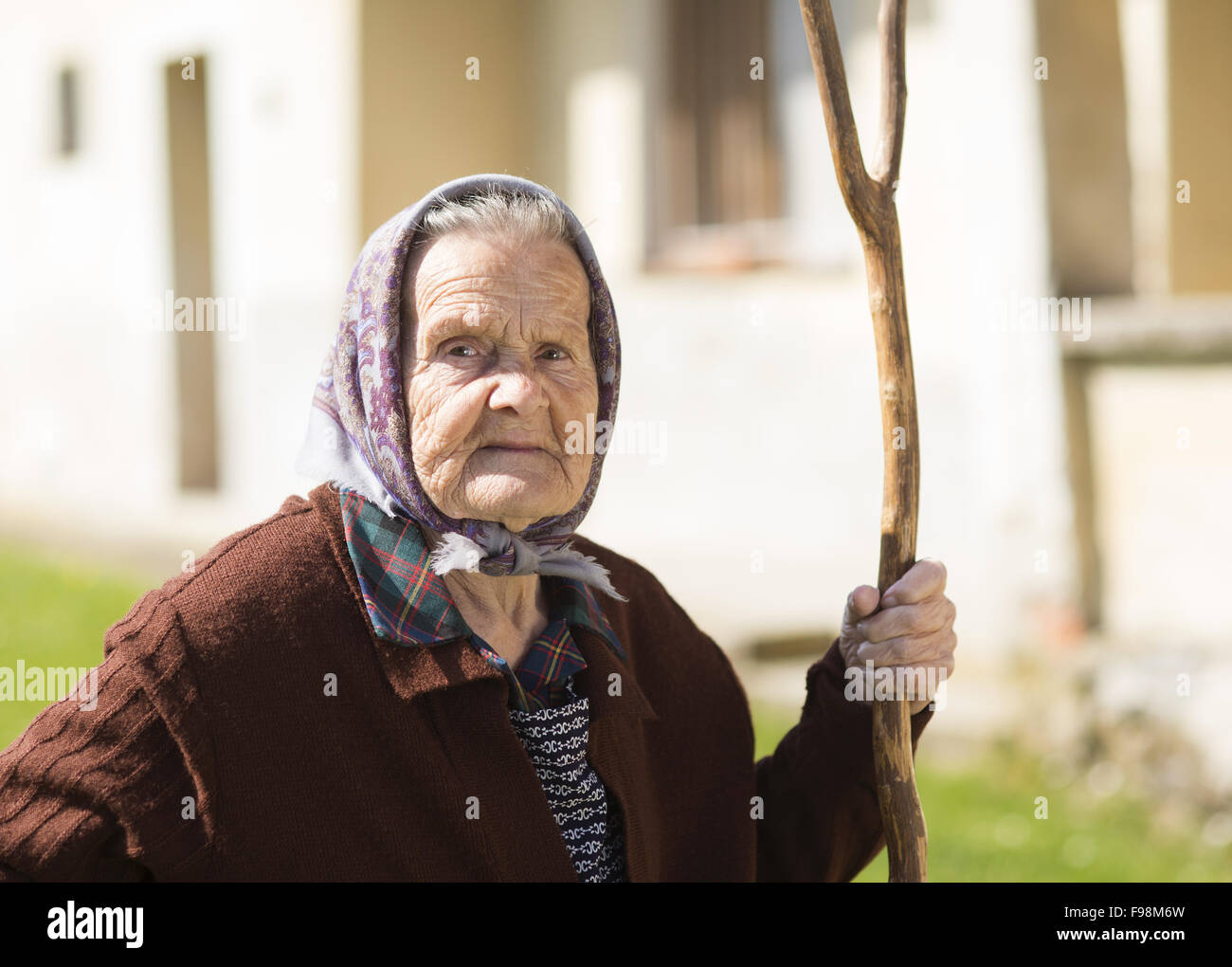 Sehr alte Frau im Kopftuch mit Rechen in ihrem Hinterhof Stockfoto