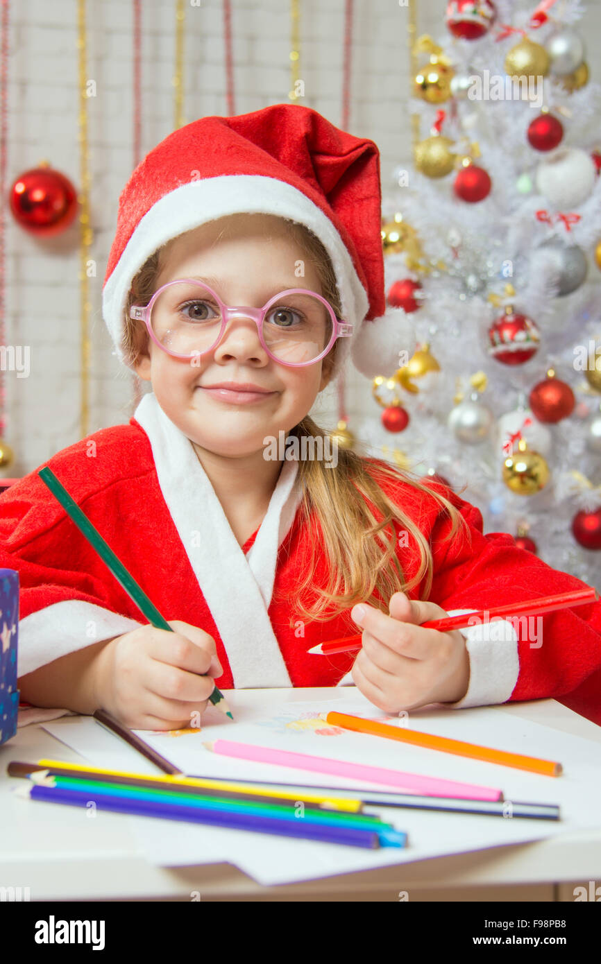 Vierjährige Mädchen gekleidet in einen roten Anzug Weihnachtsmann Ziehungen sind Bleistifte in eine festliche Weihnachten Innenausstattung Stockfoto