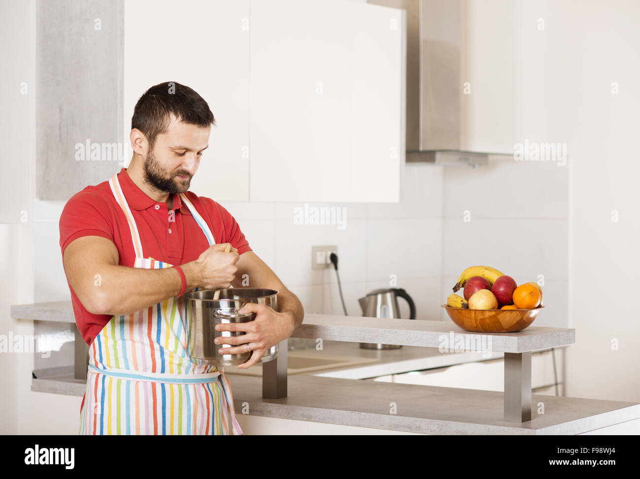 Junger Mann mit Schürze ist in der Küche kochen. Stockfoto