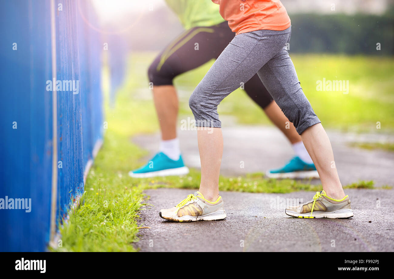 Junges Paar stretching nach dem Lauf auf Asphalt bei Regenwetter. Details der Beine. Stockfoto