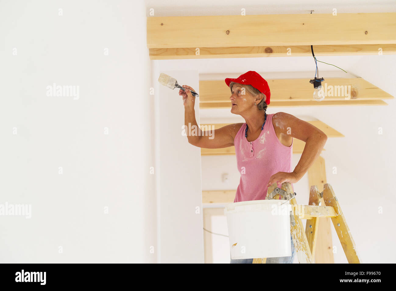 Ältere Frau Malerei Wand im neuen Haus. Sie nutzt Leiter. Stockfoto