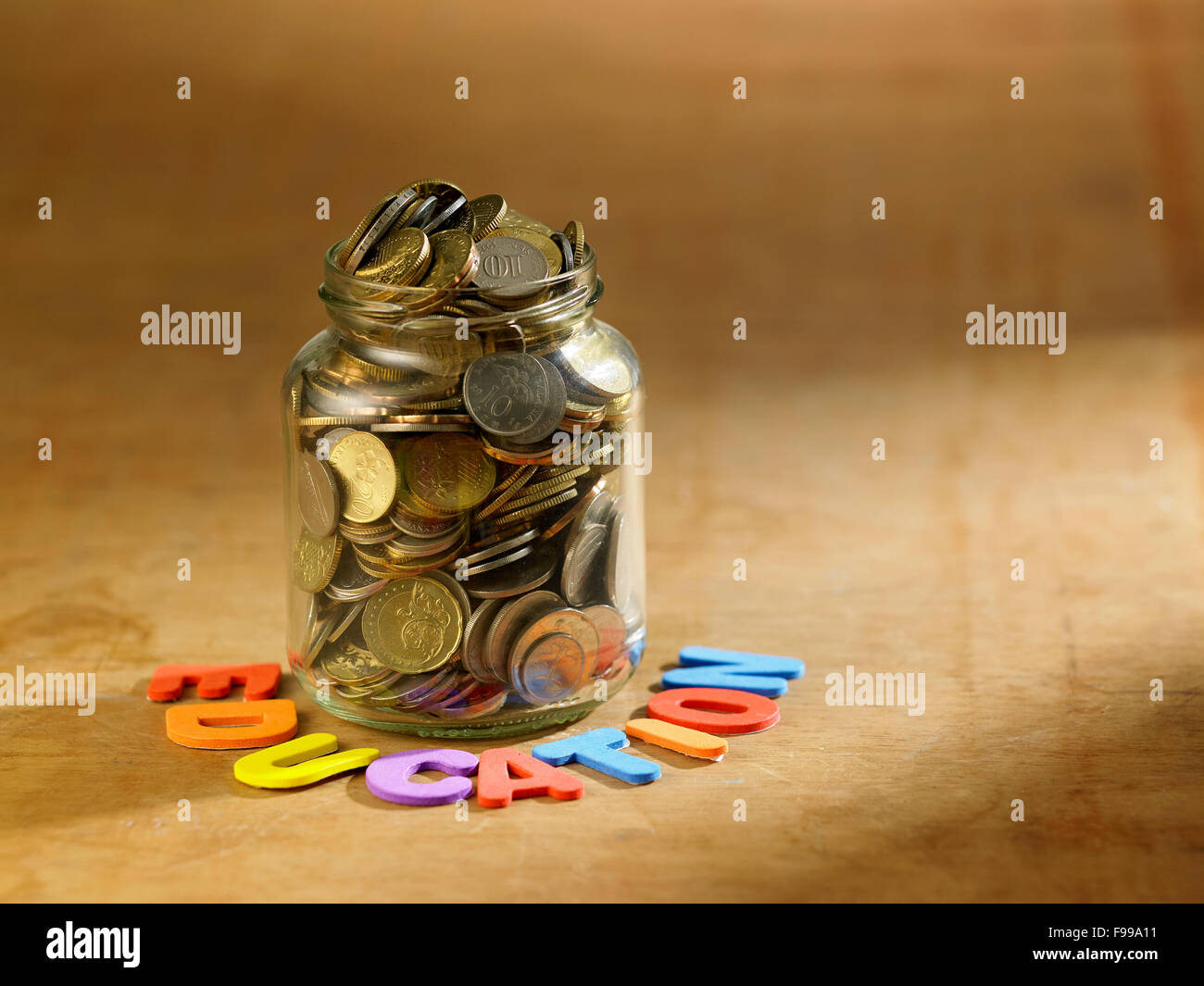 rettende Glas voller Münzen auf Holztisch Stockfoto