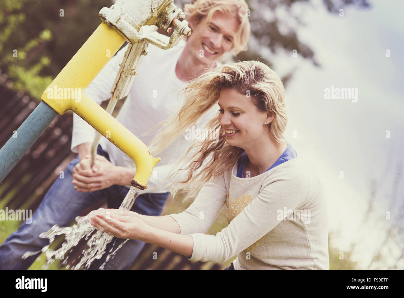 Frühling im freien Porträt des jungen Brautpaares Pumpen von Wasser aus der Wasserpumpe Stockfoto