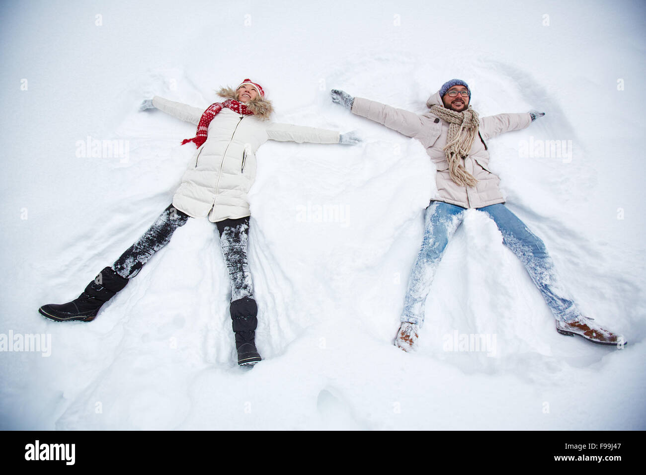 Glückliches Paar in Winterbekleidung Lügen in Schneewehe Stockfoto