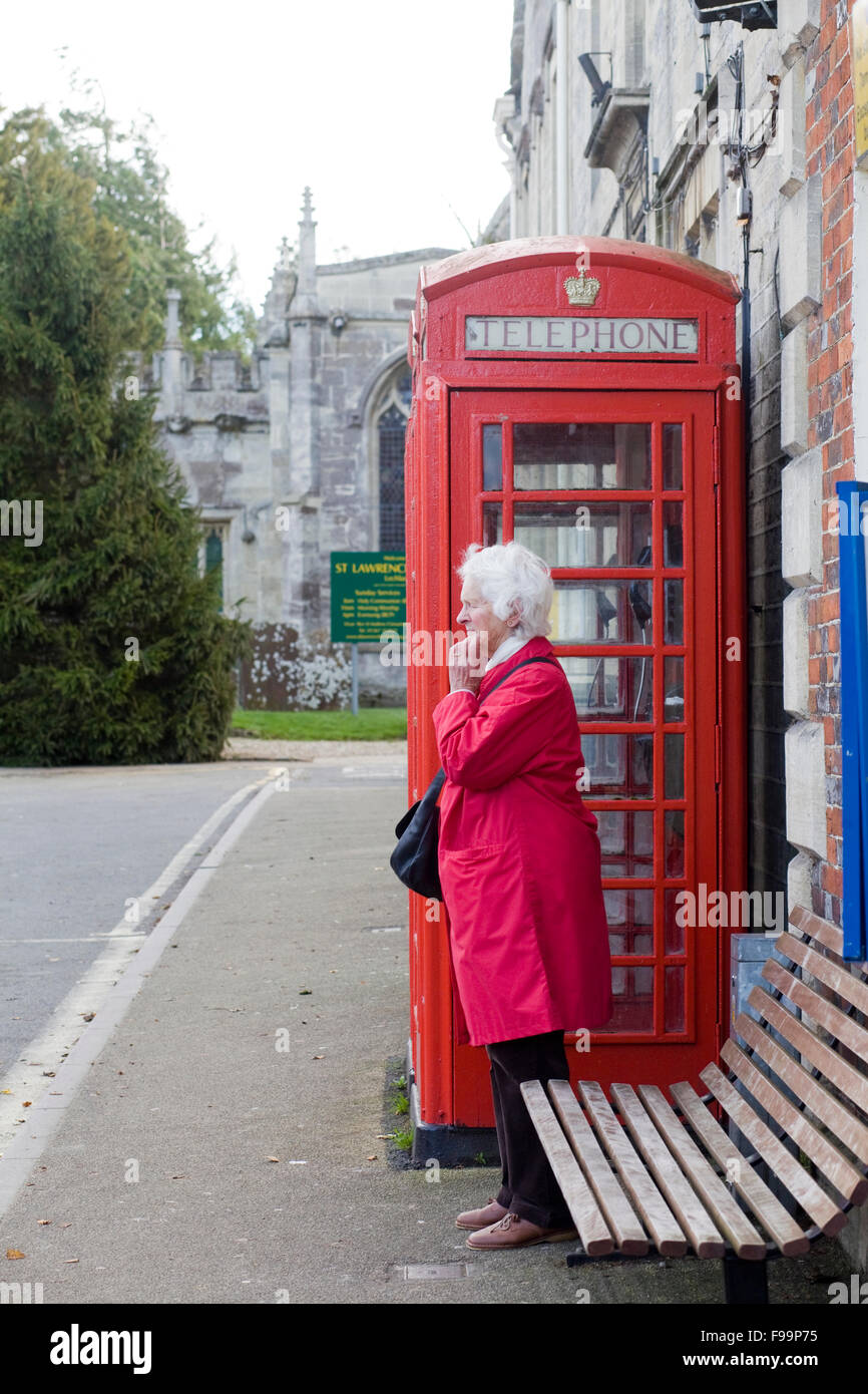 Lady in einen roten Wintermantel stand eine rote Telefonzelle einen lokalen  Bus warten Stockfotografie - Alamy