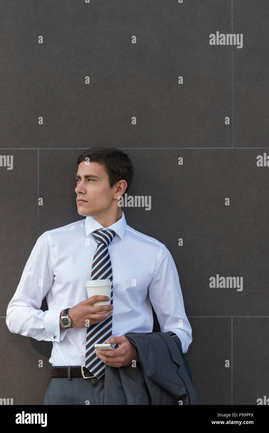 Geschäftsmann, stützte sich auf moderne Bürogebäude Wand mit Kaffee mit Handy Stockfoto