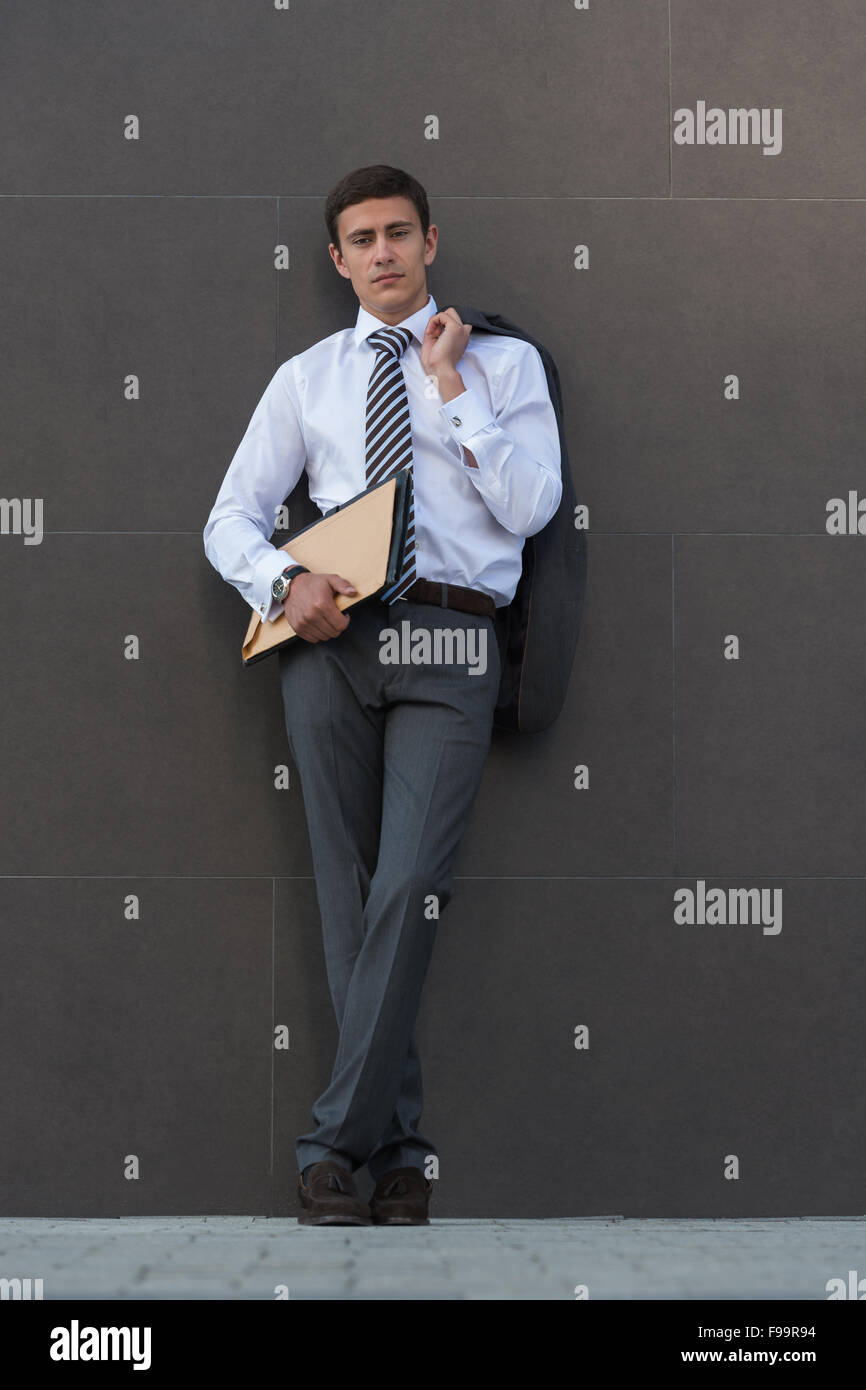 Im Geschäft Gedanken verloren. Nachdenklich Geschäftsmann in festlich gekleidet, Unterlagen und wegsehen stehend gegen grau w Stockfoto