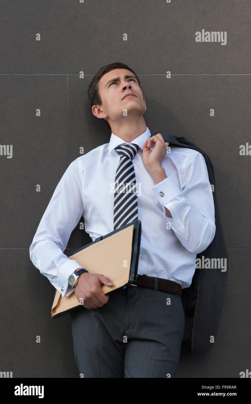 Im Geschäft Gedanken verloren. Nachdenklich Geschäftsmann in festlich gekleidet, Unterlagen und wegsehen stehend gegen grau w Stockfoto