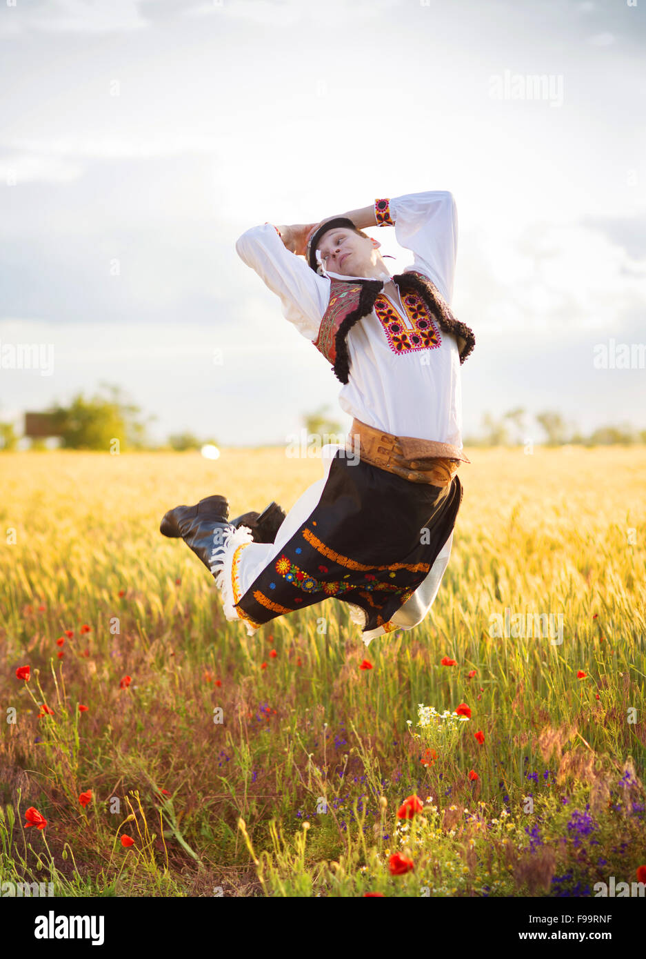 Mann im Sonnenuntergang Feld springen. Er ist Osteuropa Trachten tragen. Stockfoto