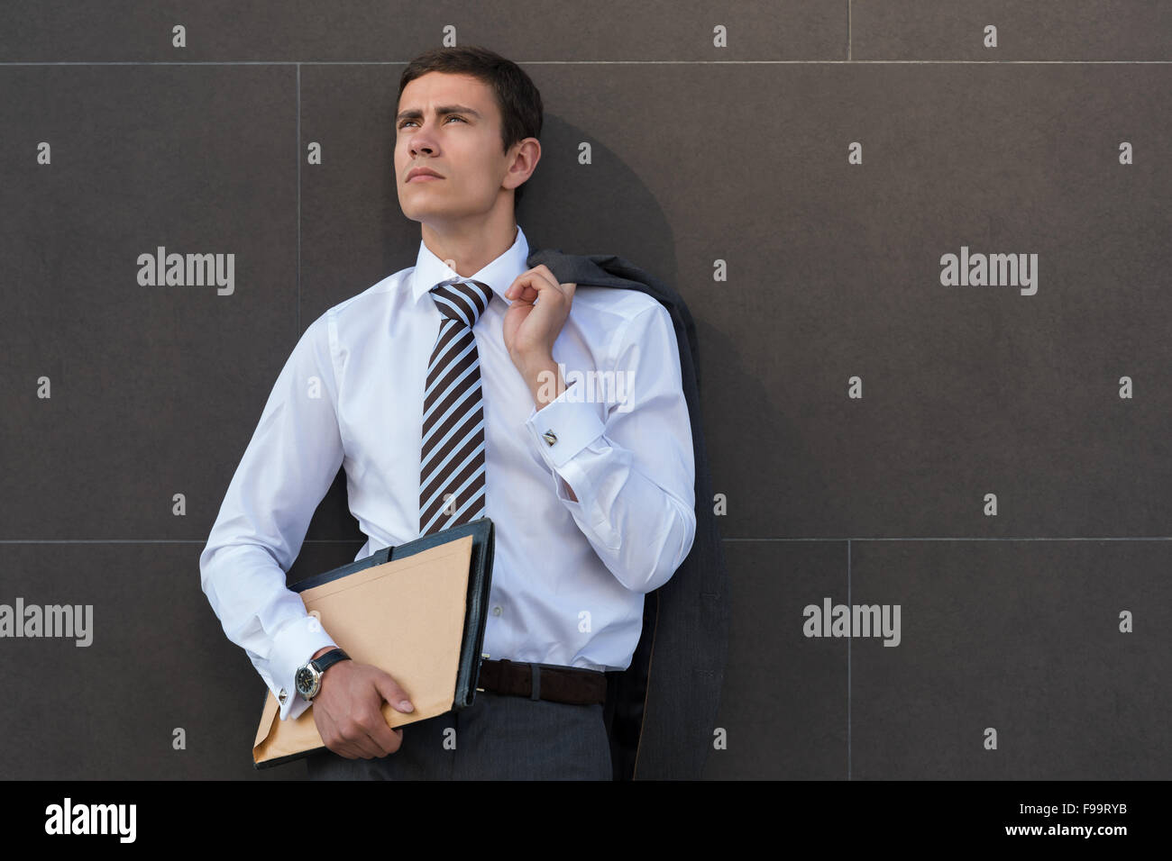 Im Geschäft Gedanken verloren. Nachdenklich Geschäftsmann in festlich gekleidet, Unterlagen und wegsehen stehend gegen grau w Stockfoto